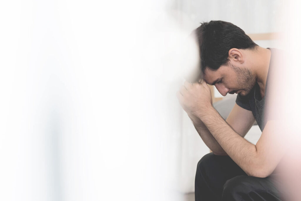 Image of an anxious man resting his elbows on his knees looking down. Work on embracing your anxiety and better manage your symptoms with the help of a holistic anxiety therapist in Hermosa Beach, CA.