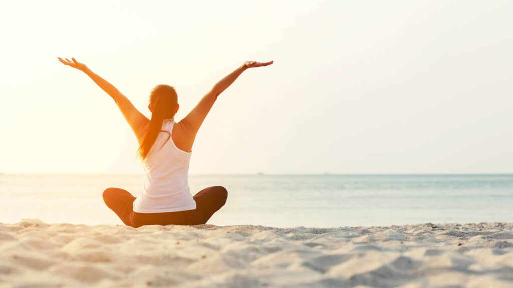 Image of a woman sitting on the beach with her hands up. This image represents the freedom you can feel after healing from your anxiety in anxiety therapy in Hermosa Beach, CA.