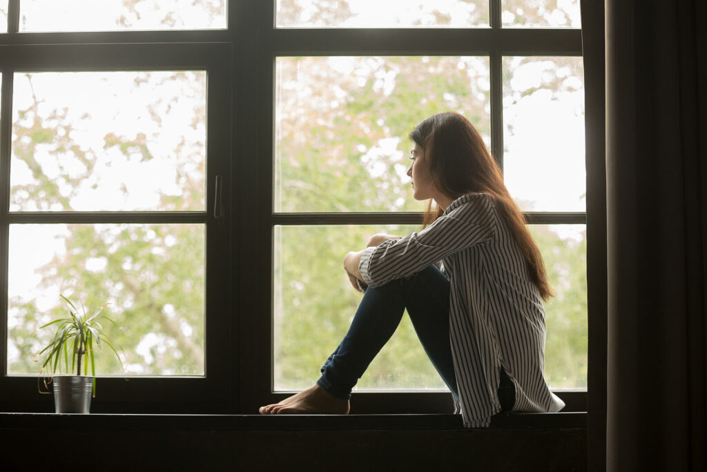 Image of a woman sitting in a window holding her knees. This image represents an anxious woman looking for holistic techniques to manage her anxiety. Learn how anxiety therapy in Hermosa Beach, CA can help you.