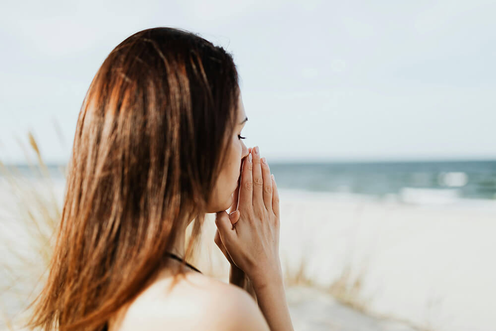 Image of a woman on a beach holding her hands to her mouth. Find the coping skills you need with the help of life transition therapy in Hermosa Beach, CA.