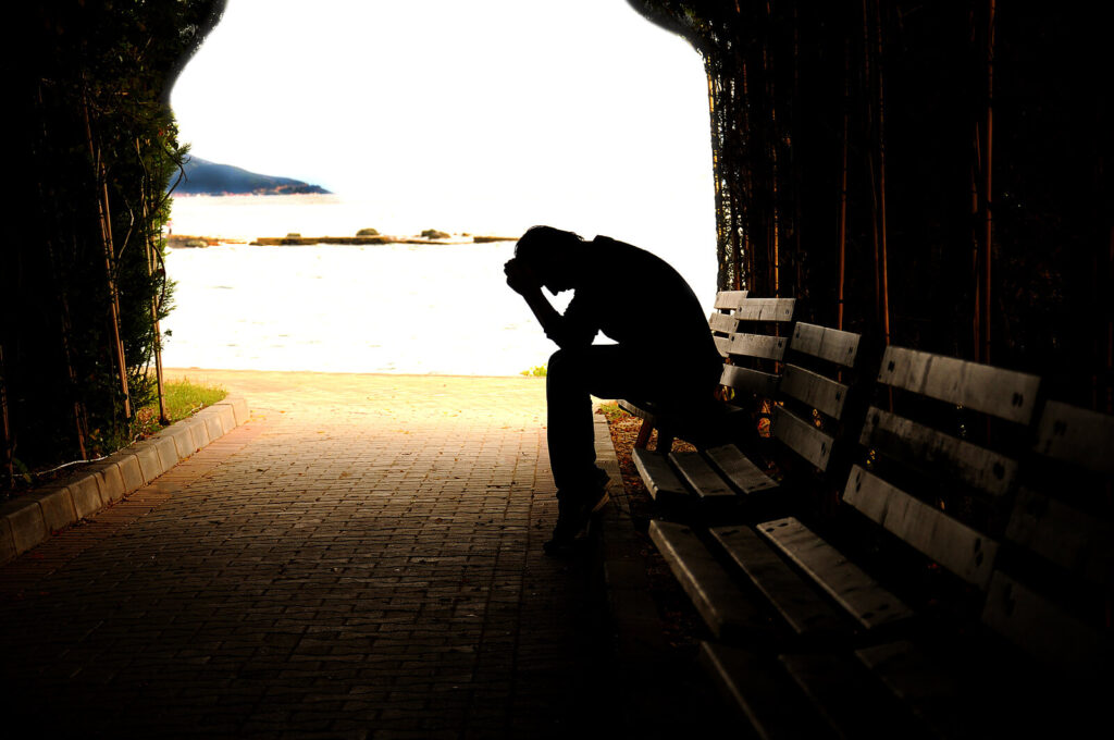 Image of an anxious man leaning his arms on his knees while sitting on a bench in a dark tunnel. If you struggle with anxiety, learn holistic ways to cope with your symptoms. Find more support with anxiety therapy in Hermosa Beach, CA.