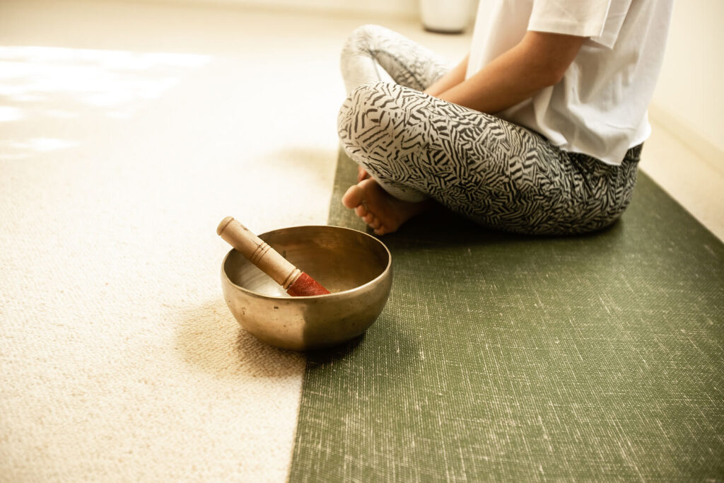 Image of a woman sitting on the floor cross-legged with a sound bowl. Find natural ways of healing from your anxiety with the help of anxiety therapy in Hermosa Beach, CA.