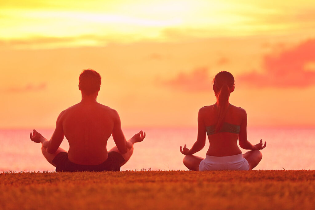 Image of a man and woman sitting on the ground practicing yoga during sunrise. Begin releasing tension and stressful emotions with the help of life transition therapy in Manhattan Beach, CA if your are dealing with a major life change.