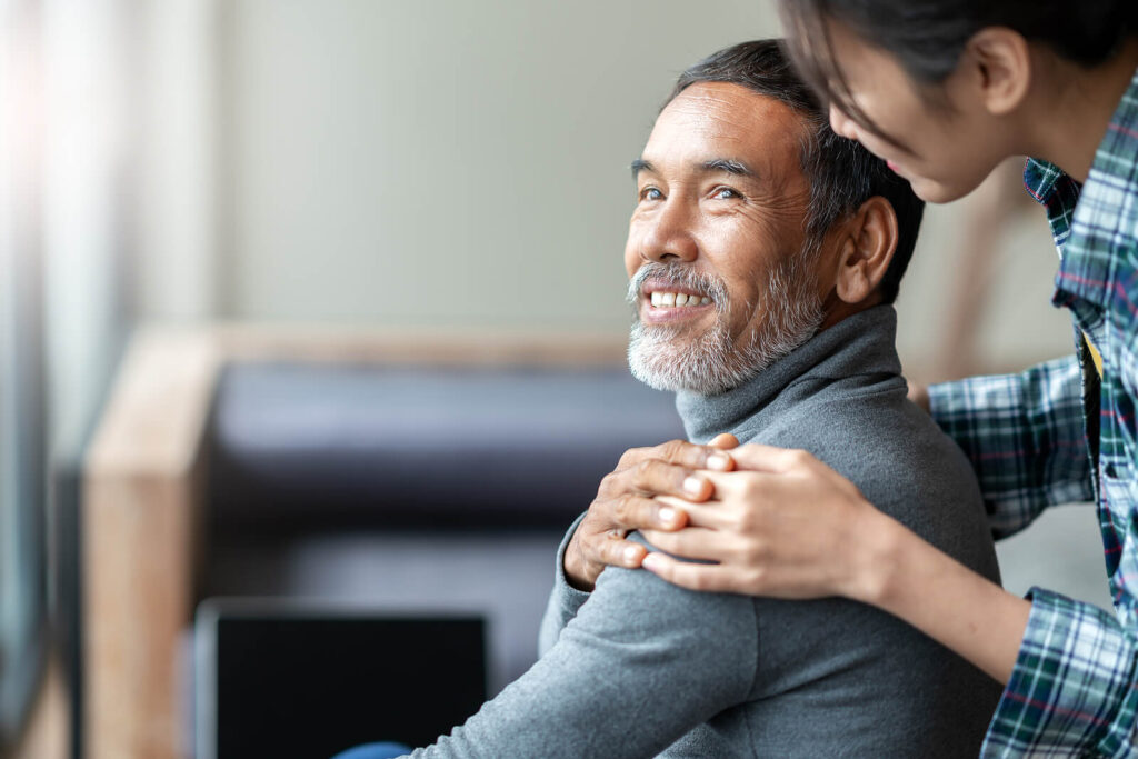 Image of a young woman resting her hand on a smiling older man's shoulder. Find balance when it comes to managing your family and aging parents with the help of life transition therapy in Manhattan Beach, CA.