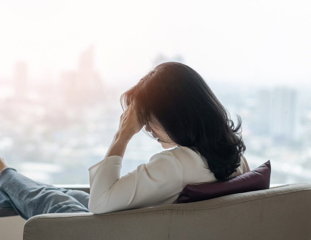 Image of an anxious woman touching her forehead while sitting on a couch. If anxiety is keeping you from living your daily life, find support with anxiety therapy in Manhattan Beach, CA. 