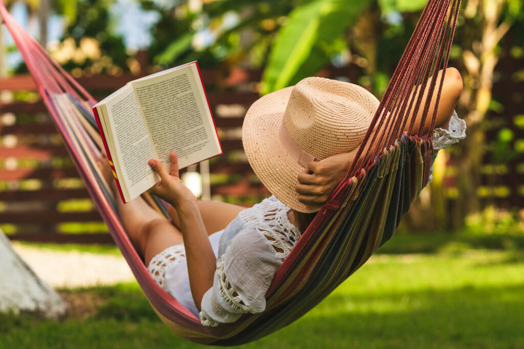 Image of a relaxed woman laying in a hammock on a sunny day reading. With the help of anxiety therapy in Manhattan Beach, CA you can begin recognizing and coping with your high functioning anxiety symptoms.