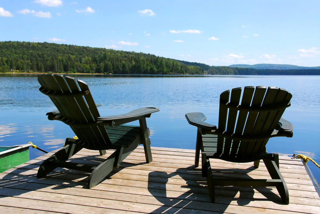 Two Adirondack wooden chairs on dock facing a blue lake with cloud reflections. Develop holistic approaches to anxiety you need to heal from your symptoms with anxiety therapy in Manhattan Beach, CA.