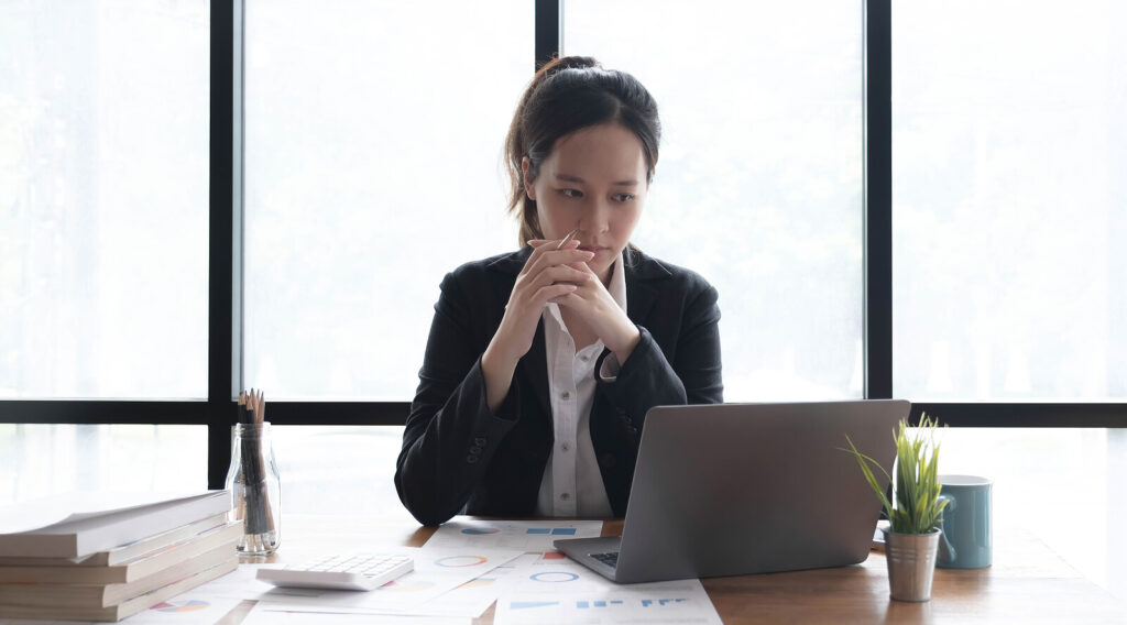 Image of an anxious professional woman clasping her hands and looking at a laptop. If you struggle with coping with your high functioning anxiety in healthy ways, discover how a skilled anxiety therapist in Manhattan Beach, CA can help.