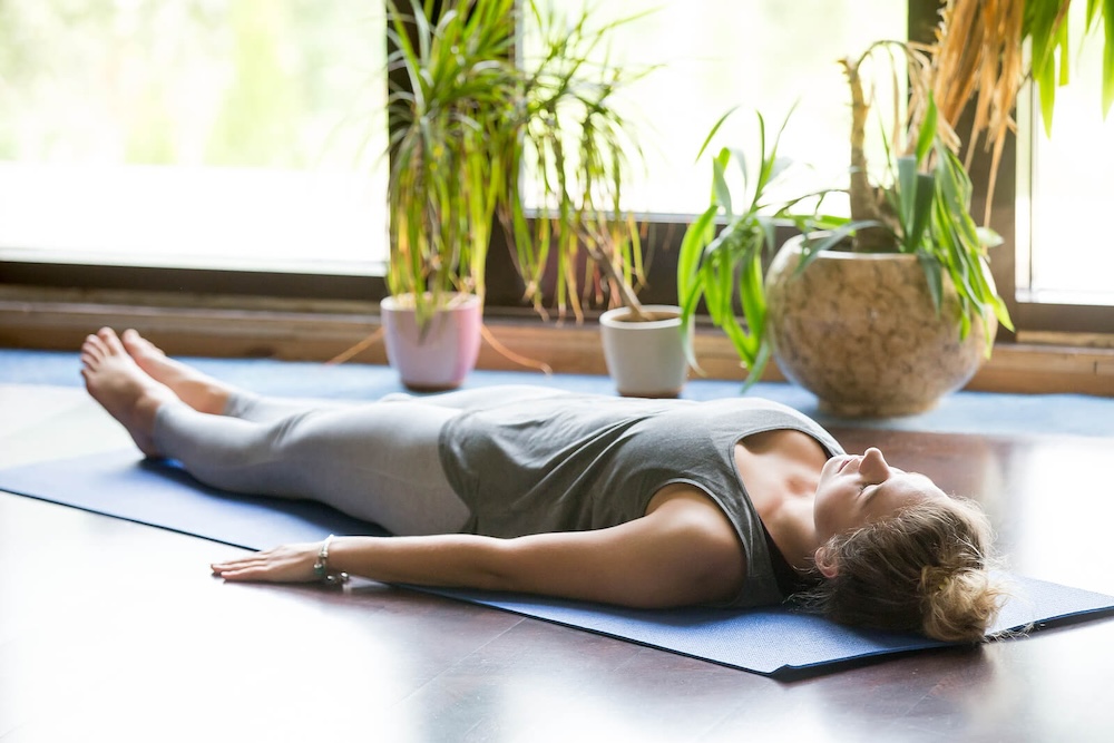 Image of a woman laying on a yoga mat on the floor practicing grounding. If you are looking to treat your anxiety holistically, discover how Marilyn Ashley, LMFT a skilled anxiety therapist in Manhattan Beach, CA can help you!