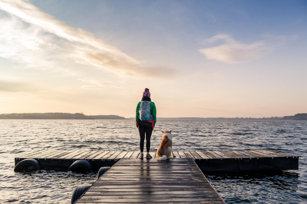 Image of a woman standing at the end of a dock with her dog. If you are looking to overcome your anxiety symptoms in healthy ways, find support with a skilled holistic anxiety therapist in Manhattan Beach, CA.