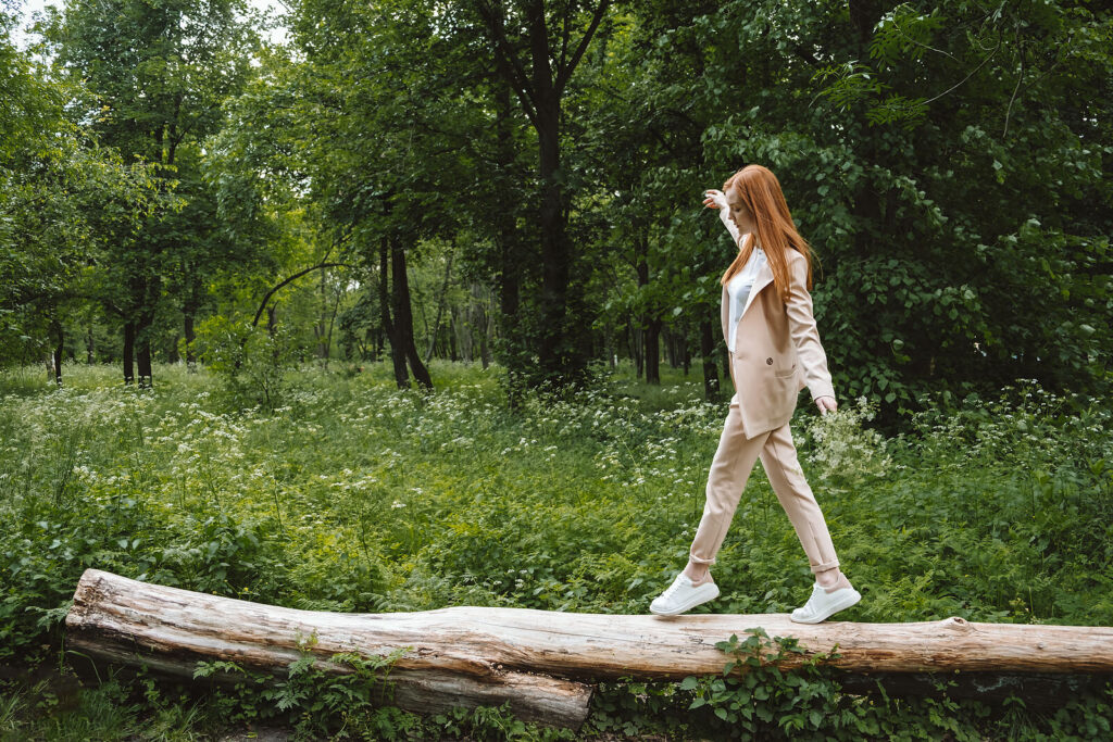 Image of a redheaded woman balancing on a log in the forest. With the support of an anxiety therapist, anxiety therapy in Manhattan Beach, CA can help you cope and balance with your anxiety symptoms.