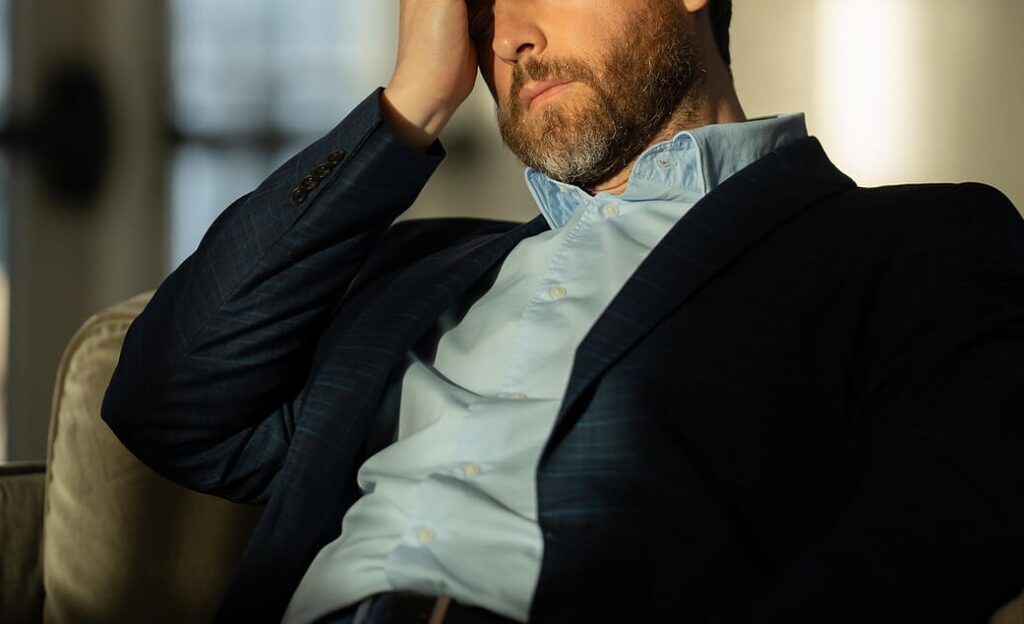 Image of an upset man closing his eyes and resting his head on his hand. Overcome the anxiety you face due to trauma with a skilled anxiety therapist in Manhattan Beach, CA.